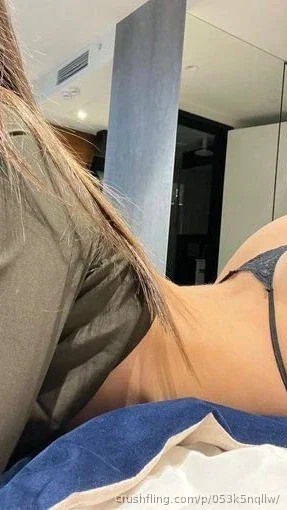 Woman with long hair in dark lingerie lying on bed indoors.