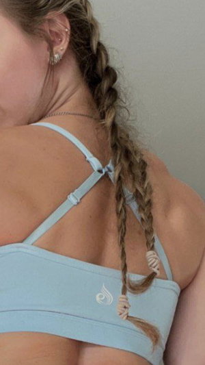 Woman with braided hair wearing light blue sports bra, back view, indoor setting.