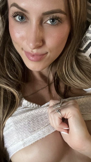 Blonde woman pulling white lace top low, cleavage, bedroom.