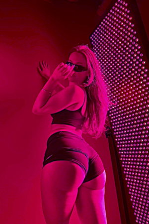 Blonde woman in black athletic wear posing indoors with red lights.