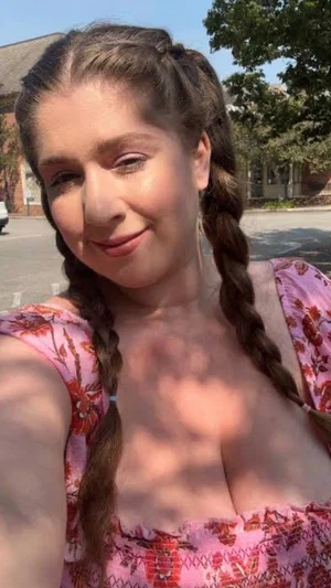 Woman with braided hair in floral top, outdoors in daylight.