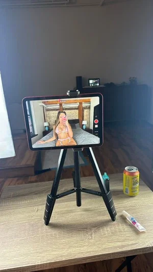 Woman in pink lingerie posing on bed, viewed on tablet screen in bedroom.