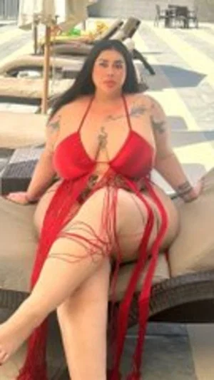 Woman with tattoos in red string bikini sitting on outdoor lounge chair.