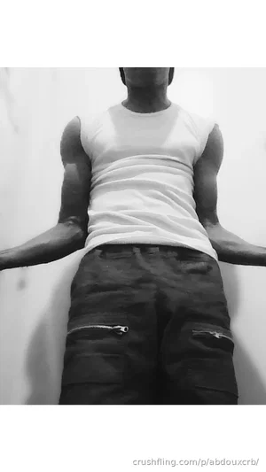 Man in white tank top and dark pants standing against a wall, arms outstretched.