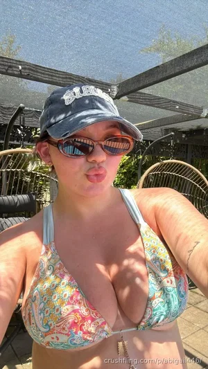 Woman in colorful bikini top and cap posing outdoors under shade.