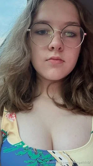 Woman with wavy hair and round glasses wearing a colorful tank top, close-up selfie.