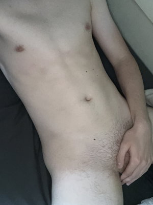 Shirtless slim man lying down with hand covering crotch.