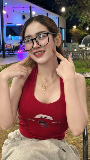 Asian woman in red tank top and glasses posing outdoors at night.