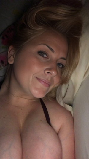 Blonde woman in black bra on bed.