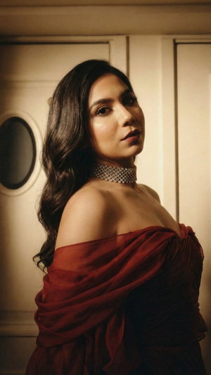 Woman with long dark hair in off-shoulder red dress, wearing sparkly choker, indoors.