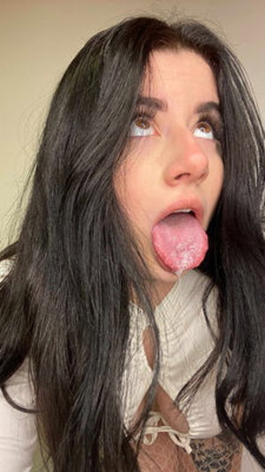 Woman with long dark hair sticking out tongue indoors.