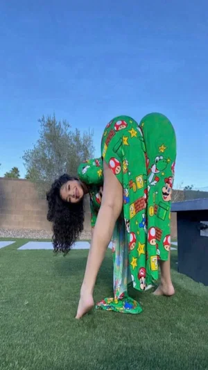 Woman in green Mario-themed pajamas bending forward on grass outdoors.