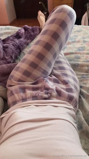 Person in checkered pants and light top lying on bed, legs raised, purple blanket nearby.