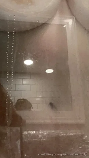 Foggy bathroom mirror reflecting shower area with tiled walls and ceiling lights.
