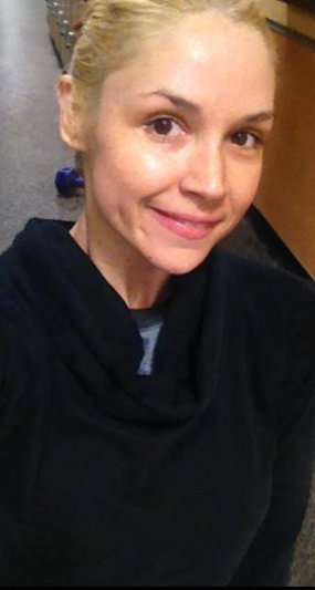 Blonde woman in black cowl neck sweater, smiling, indoor setting.