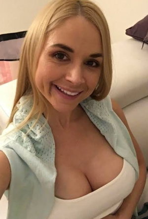 Blonde woman in white top with light blue cover, smiling in indoor setting.