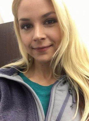 Blonde woman in teal shirt and gray hoodie, indoor selfie.
