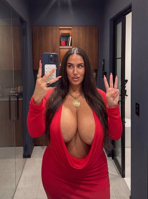 Woman in red plunging dress taking mirror selfie in modern bathroom.