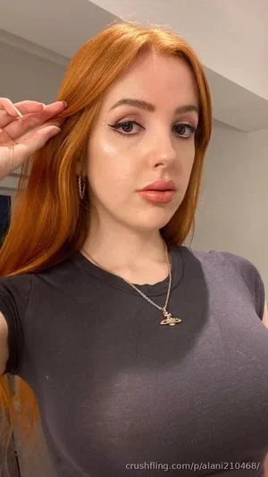 Woman with red hair wearing dark gray t-shirt and necklace, posing indoors.