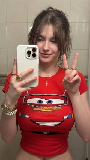 Woman in red Lightning McQueen t-shirt taking mirror selfie in bathroom.