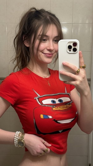 Woman in red Lightning McQueen t-shirt taking mirror selfie in tiled room.