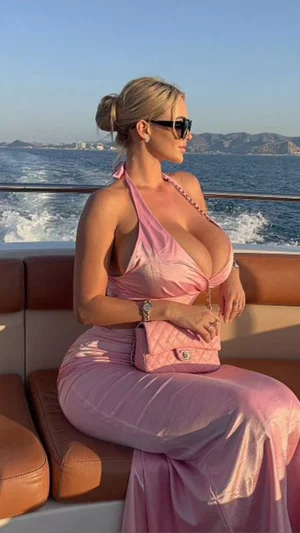 Woman in pink halter dress on boat, blonde hair in bun, wearing sunglasses.