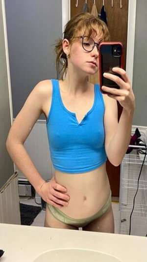 Slim woman with red hair, glasses, blue crop top, green panties in bathroom.