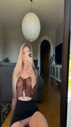 Blonde in sheer top and black mini skirt, indoor mirror selfie.