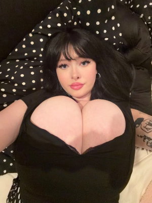Black-haired woman in low-cut top taking selfie on bed