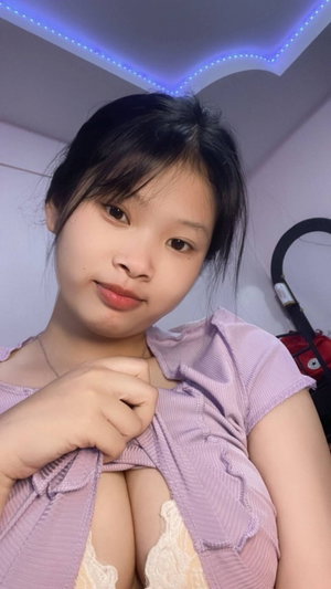 Asian woman in purple top pulling neckline indoors.