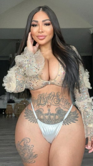 Woman with long dark hair in sheer top and white bikini indoors.