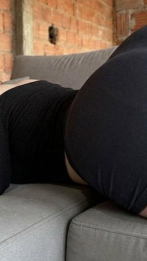 Person in black leggings lying on gray couch with brick wall background.