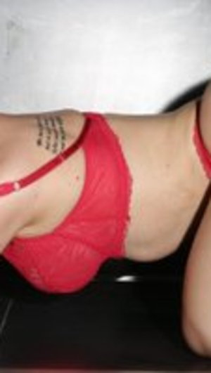 Woman in red lace lingerie posing sideways indoors.