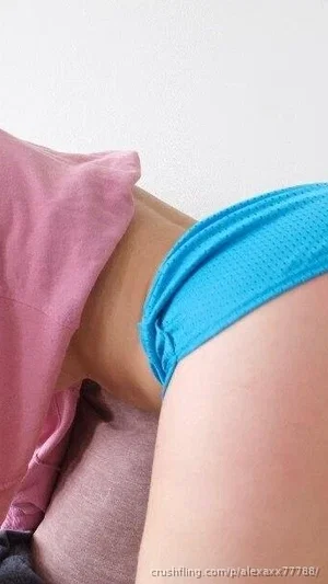 Woman in blue underwear lying on pink pillows, indoor setting.