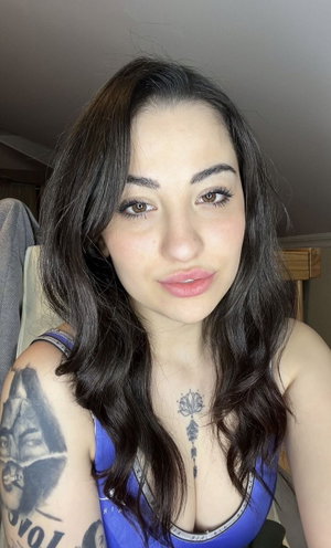 Woman with dark hair and tattoos wears a blue top, indoors.