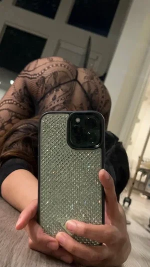 Woman in black lace bodysuit taking mirror selfie indoors, holding phone with glitter case.
