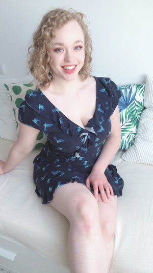 Curly blonde woman in blue dress on white couch.