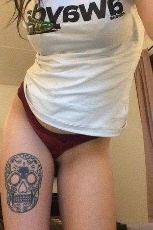 Woman in white t-shirt and maroon underwear with skull tattoo on thigh.