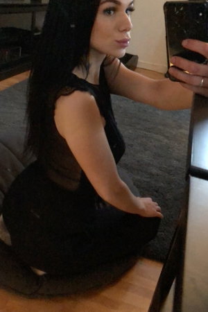 Long-haired woman in black dress taking selfie indoors.