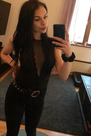 Woman with long dark hair taking mirror selfie indoors.