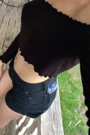 Woman in black crop top and shorts on wooden deck.