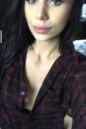 Woman with long dark hair in plaid shirt taking selfie indoors.