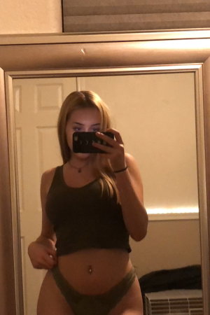 Blonde woman in green crop top and underwear taking mirror selfie indoors.
