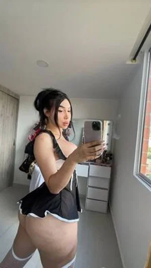 Woman in black and white outfit with thigh-high socks taking mirror selfie in room.