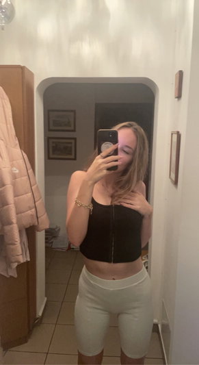 Woman in black crop top and white shorts taking mirror selfie in hallway.