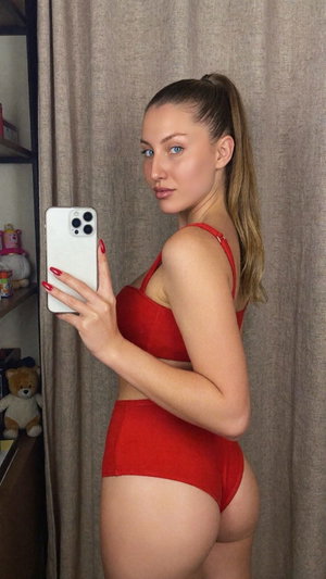 Woman with ponytail in red lingerie taking mirror selfie indoors.