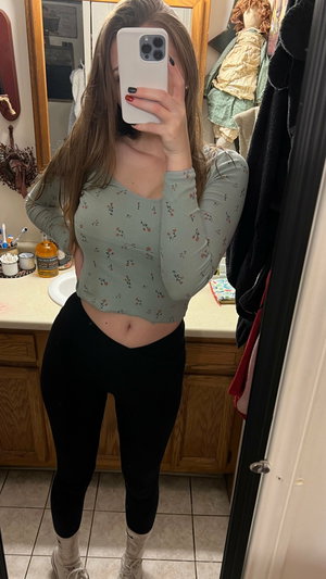 Woman taking mirror selfie in bathroom wearing floral crop top.