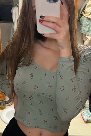 Woman in floral crop top taking mirror selfie in bathroom.