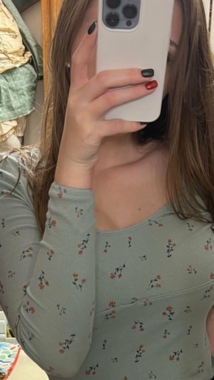 Woman with long brown hair in floral top taking mirror selfie indoors.