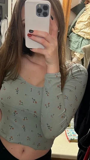 Woman in floral long-sleeve crop top, holding phone to face, indoor setting.